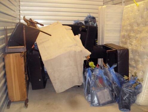 Small storage unit with couch, old dresser, and 5 bags filled with old junk